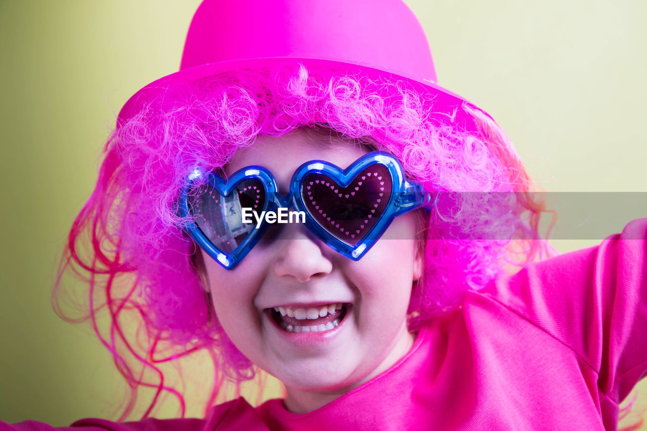 Portrait of happy girl with pink wig against yellow background
