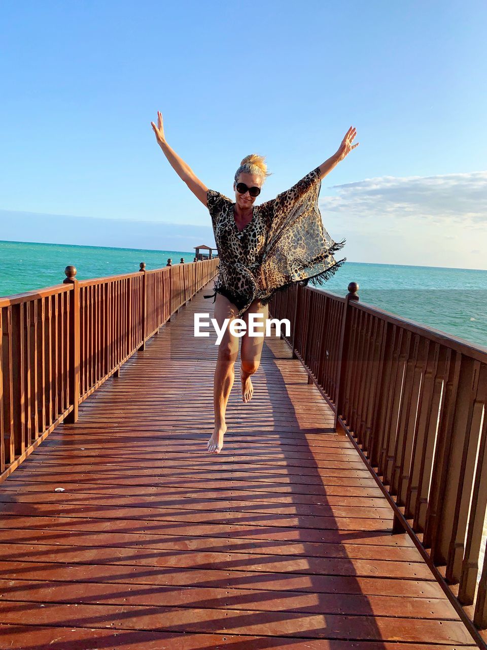 Full length of woman jumping on pier over sea against sky