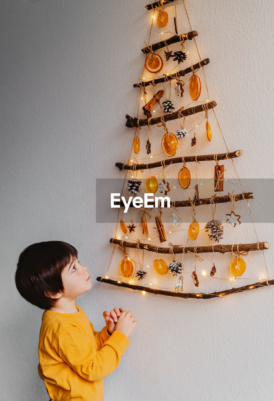 Little child looking at handmade craft christmas tree made from sticks and natural materials 
