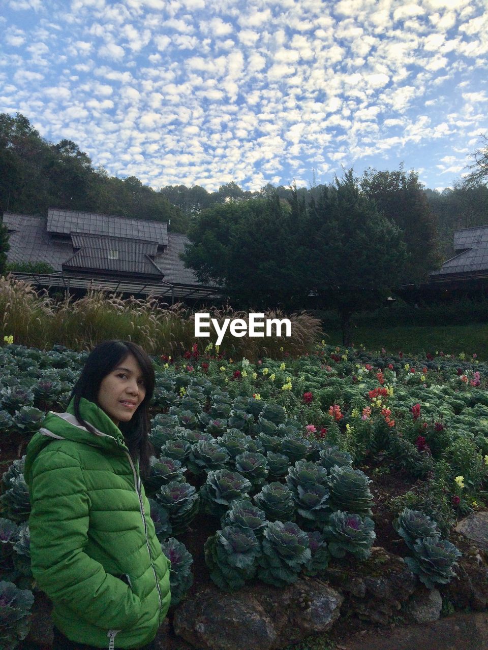 PORTRAIT OF YOUNG WOMAN STANDING BY PLANTS