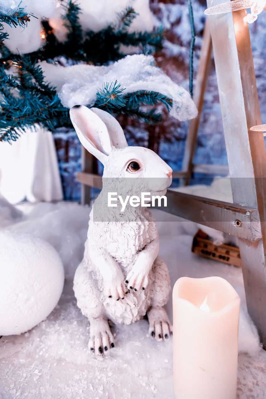 White plaster rabbit on the background of a snow-covered christmas tree 