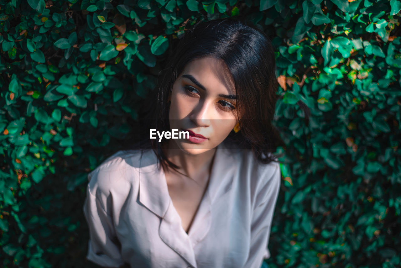 PORTRAIT OF YOUNG WOMAN STANDING AGAINST PLANTS