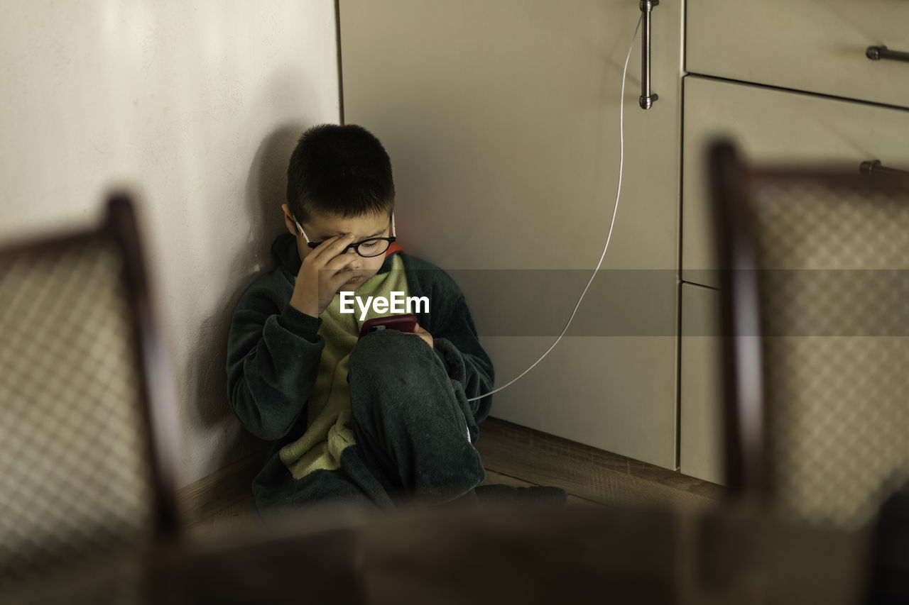 Closeup portrait of boy looking into phone sitting on the floor, playing on the phone on charging