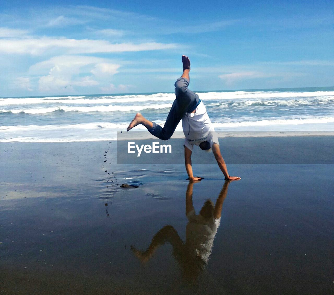 Full length of playful man practicing cartwheel on shore at beach
