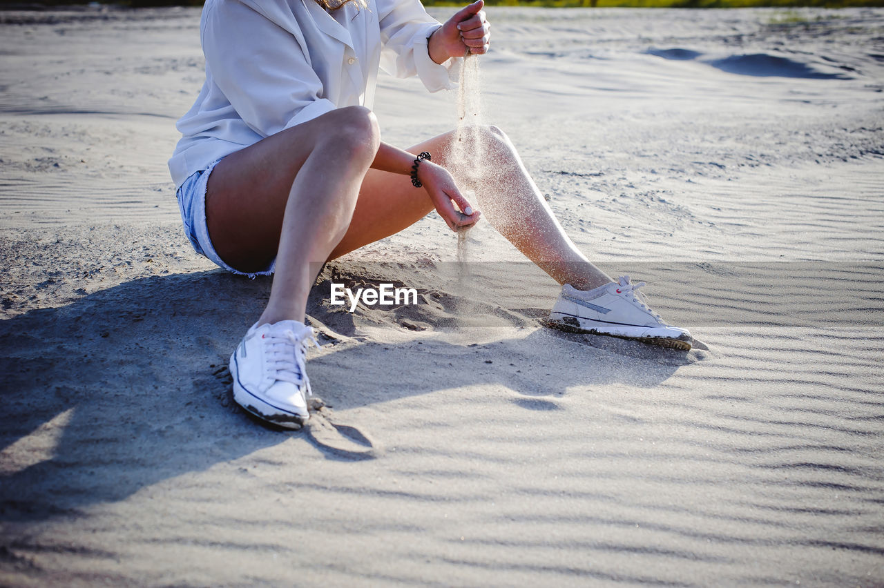 Low section of woman spilling sand at beach