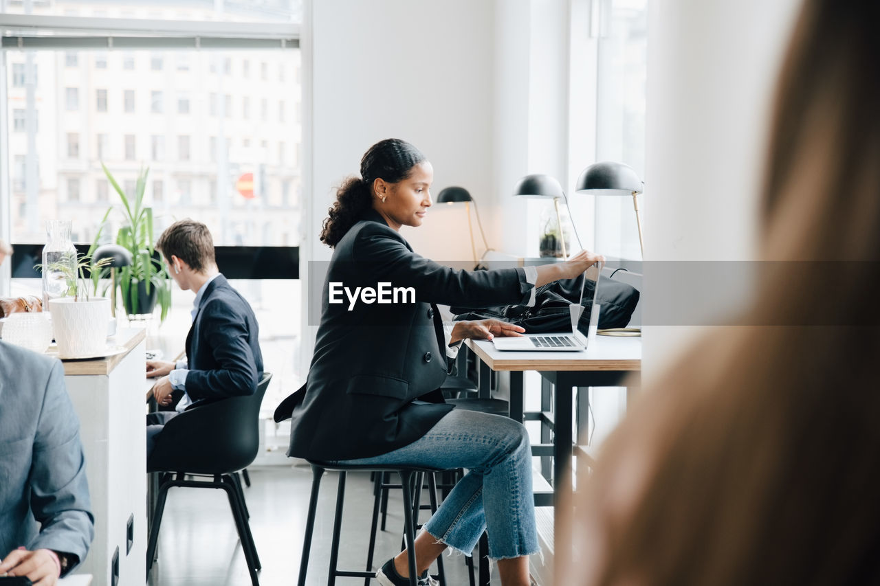 Side view of businesswoman working on laptop while sitting at desk in office cafe