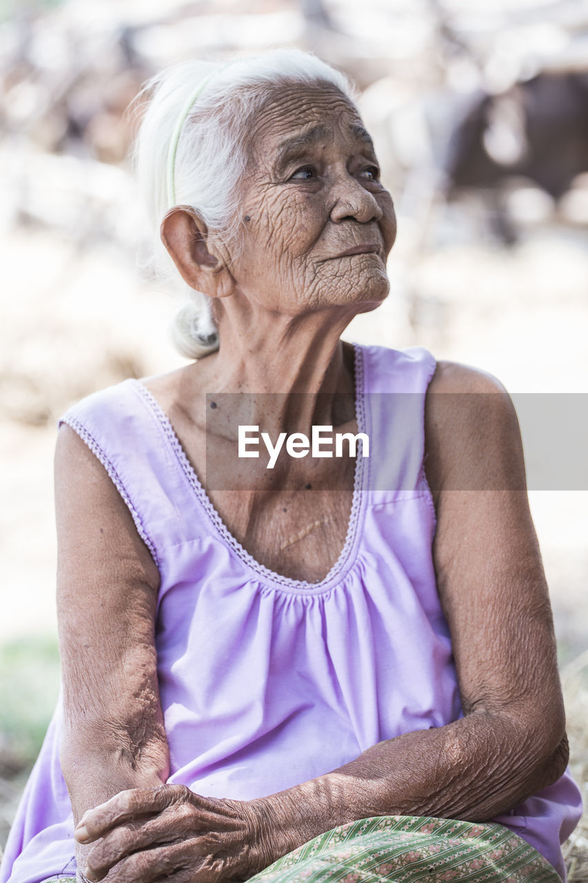 Wrinkled senior woman looking away while sitting outdoors