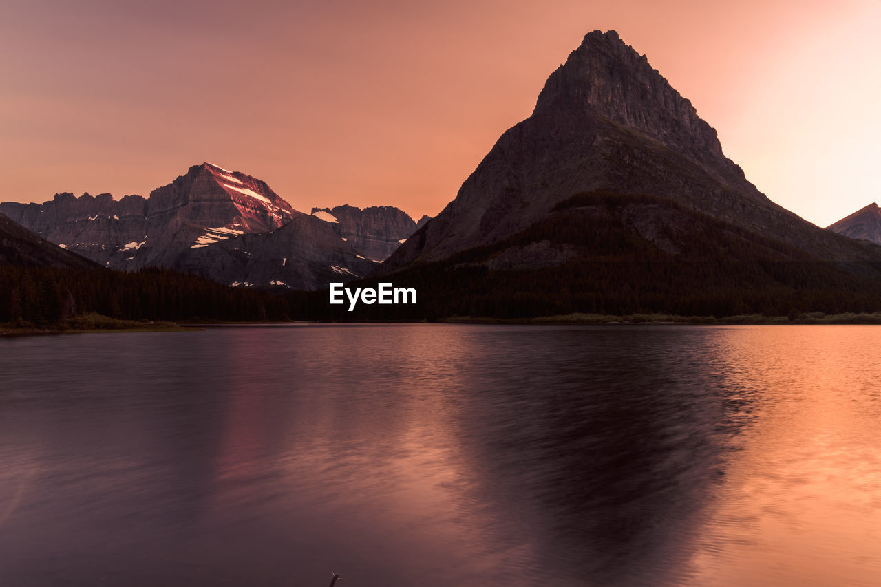 SCENIC VIEW OF LAKE BY MOUNTAINS AGAINST SKY AT SUNSET