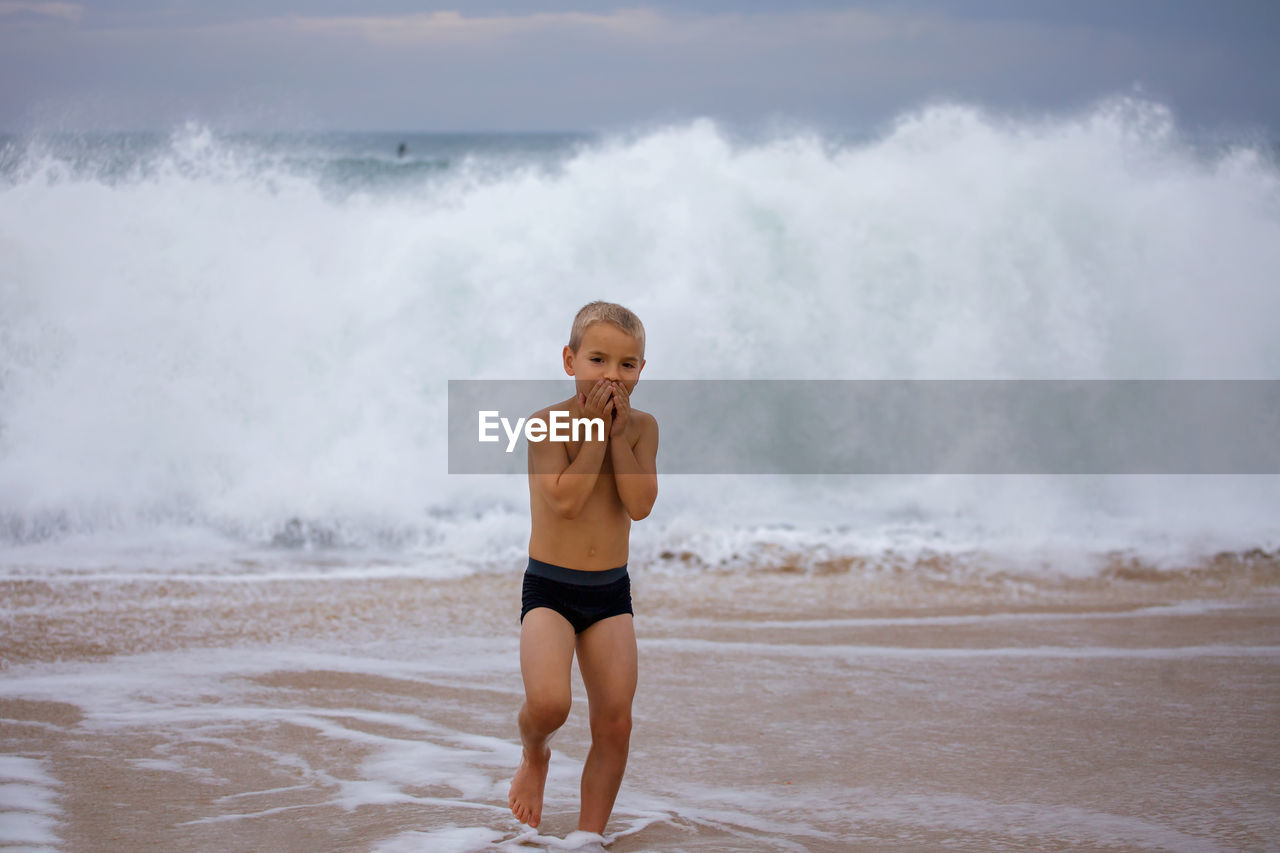 Kid plays on shore of huge, raging ocean. childhood freedom and adventure. discovery of the world