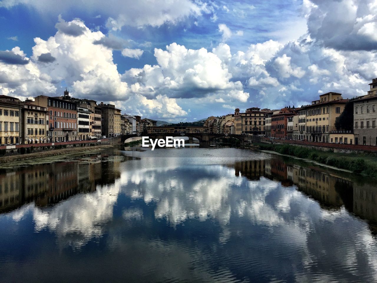 Ponte vecchio over arno river amidst buildings against cloudy sky