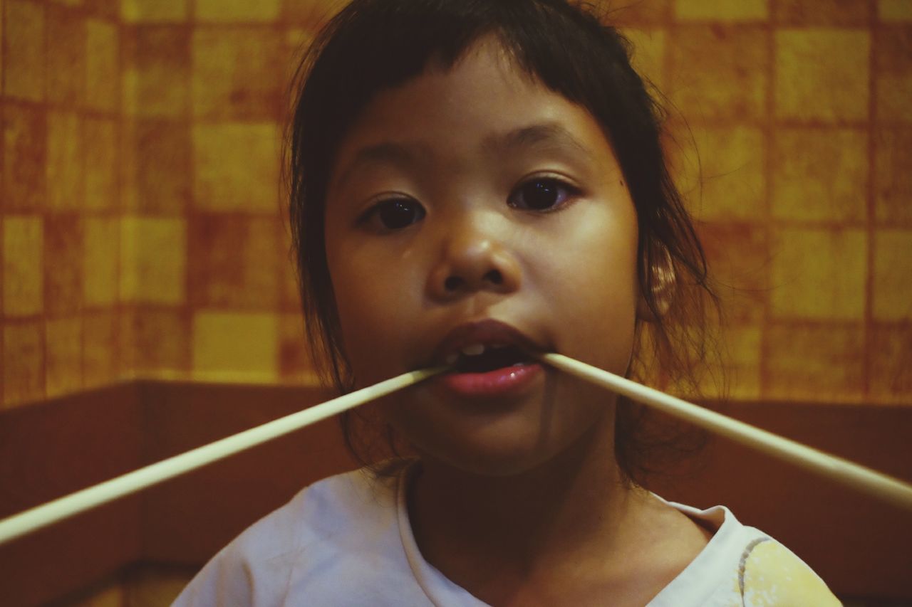 Close-up portrait of girl holding chopsticks in mouth at home