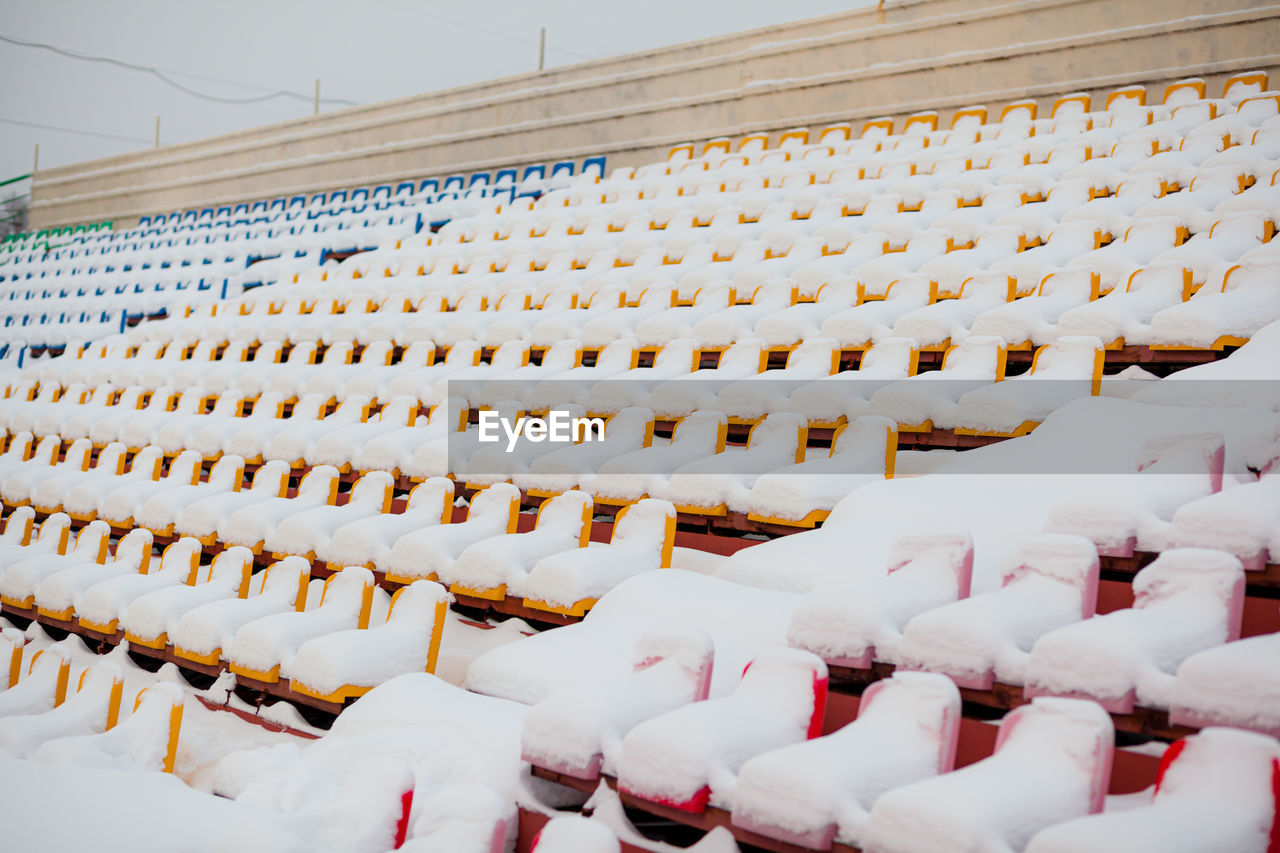 Empty outdoor football soccer stadium seats covered with snow in winter, light snowfall.