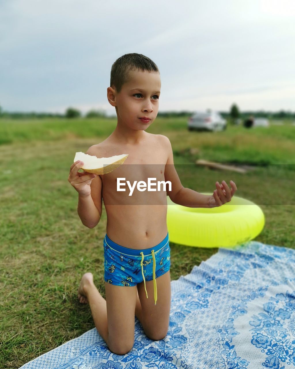 A seven-year-old child in swimming trunks eats a melon in nature