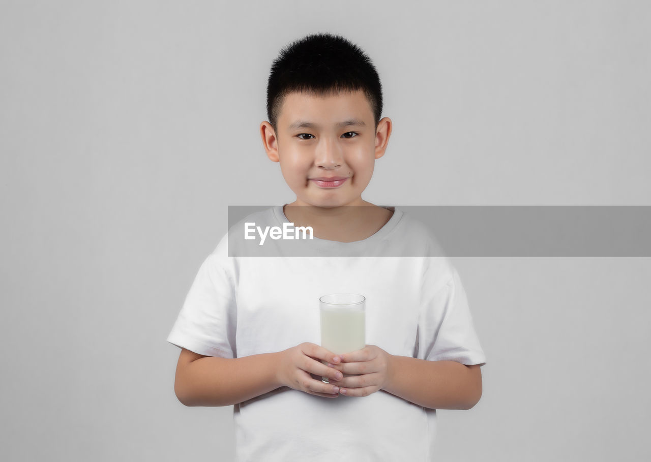PORTRAIT OF BOY HOLDING DRINK AGAINST WHITE BACKGROUND