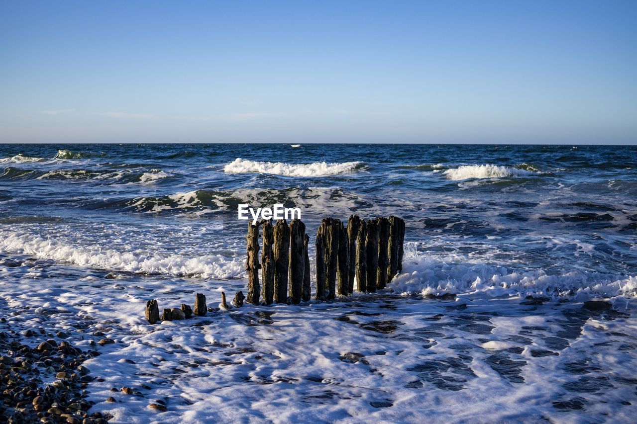 WOODEN POSTS ON BEACH AGAINST CLEAR SKY
