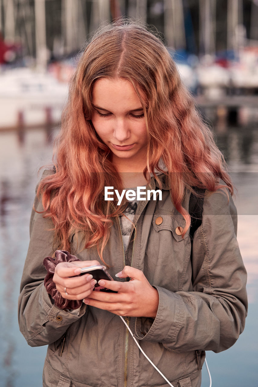 YOUNG WOMAN USING MOBILE PHONE WHILE STANDING ON CAMERA AT SMART