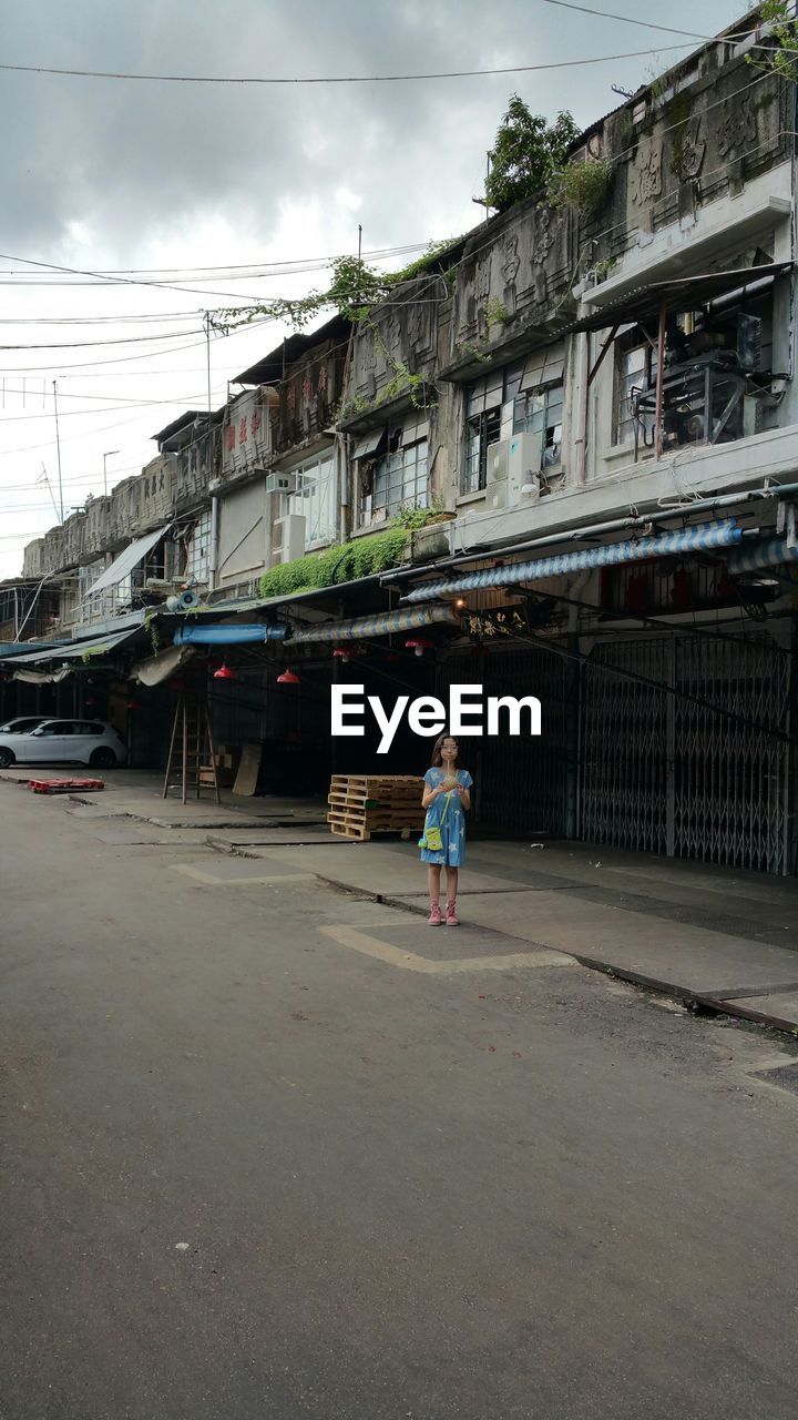 Girl standing on street against building