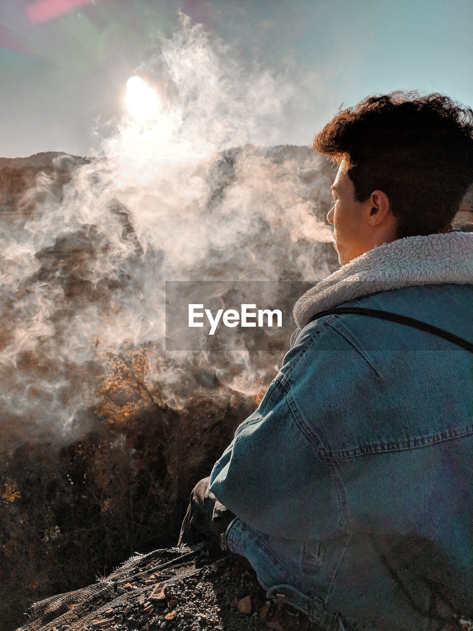 Hiker smoking cigarette while sitting on mountain
