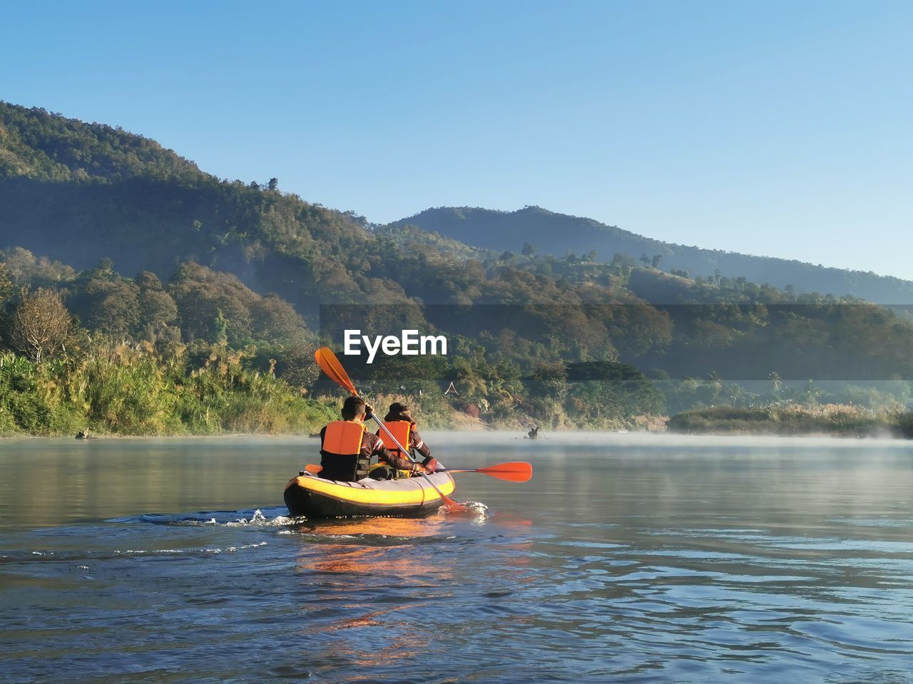 People rowing boat in lake against sky