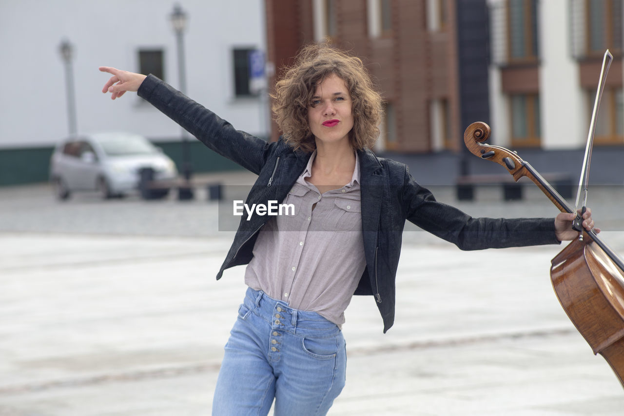 Portrait of smiling woman holding violin while dancing on street