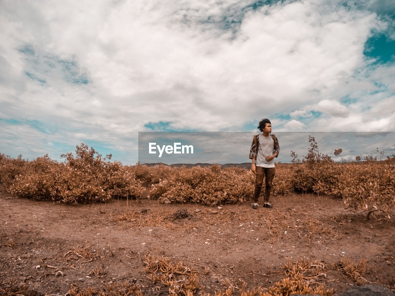 Young man standing on field against cloudy sky