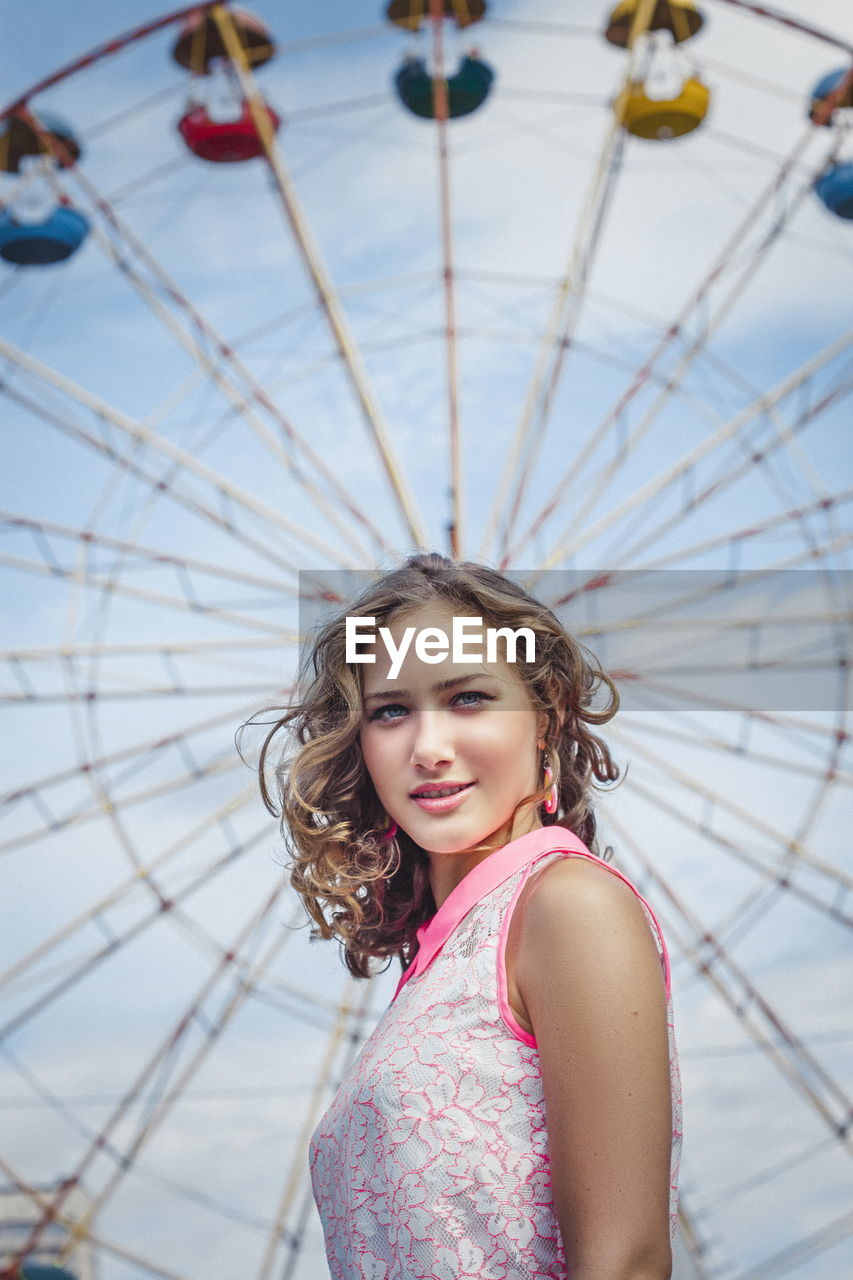 Portrait of smiling young woman standing against ferries wheel