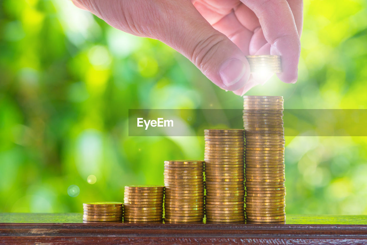 Cropped hand stacking coins on table against plants