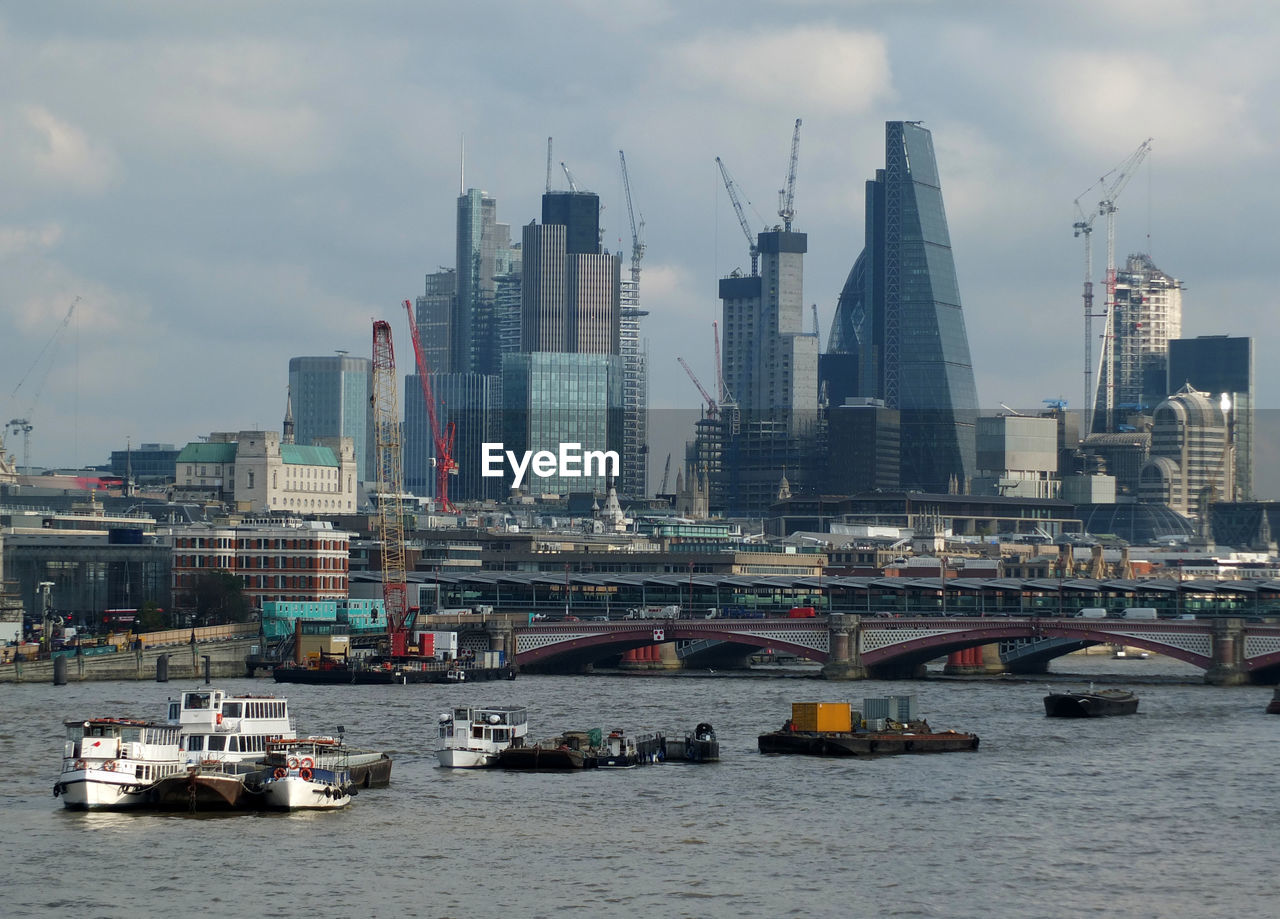 Boats in river by buildings against sky in city