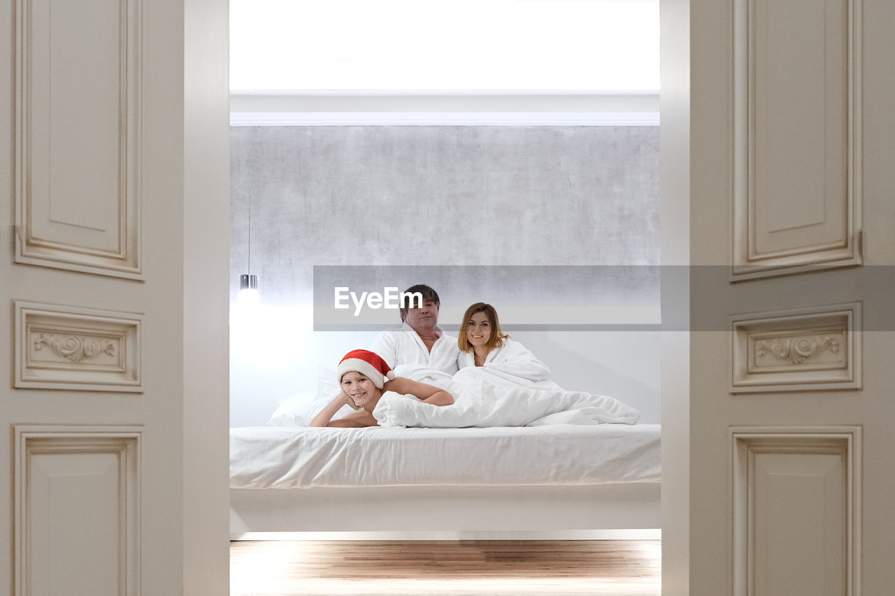 Family lies in bed waiting for santa claus for christmas. child in santa hat.