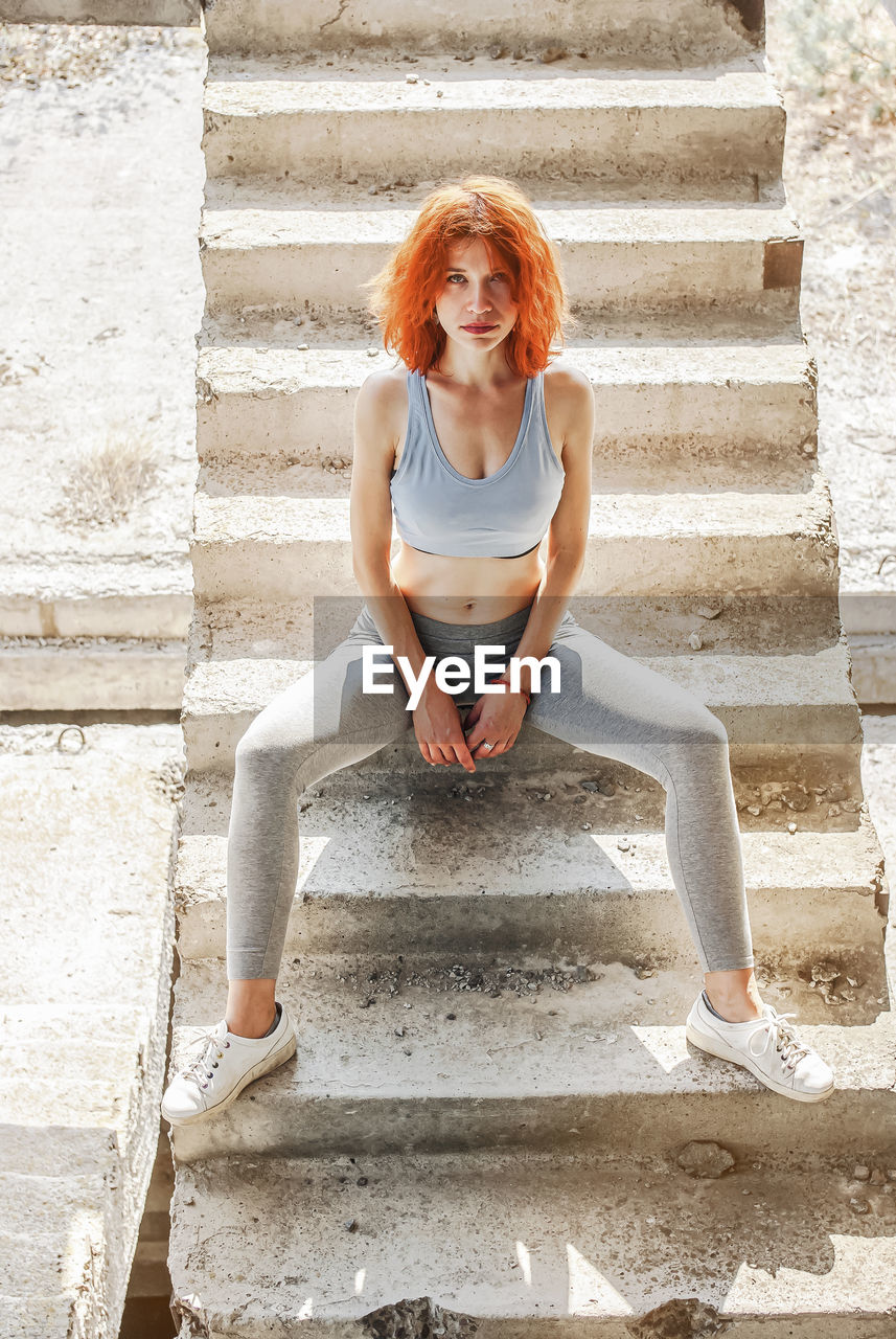 Cheerful woman, relaxing after fitness workout in park, sitting on concrete steps outdoors