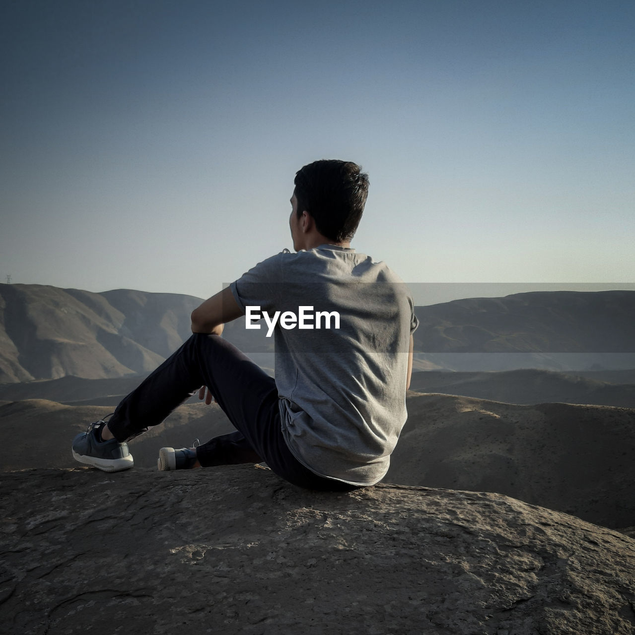 Rear view of man sitting on mountain against clear sky