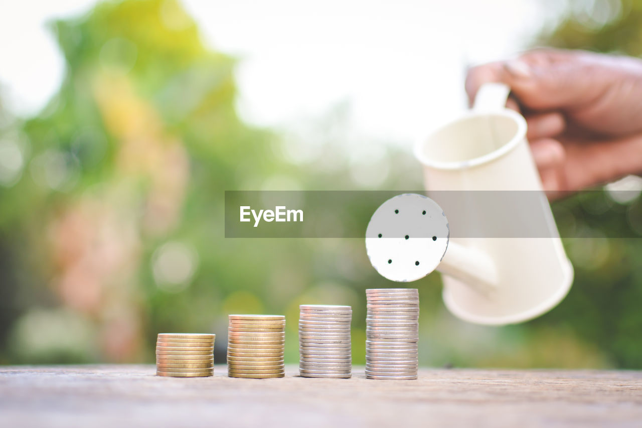 Cropped hand watering stacked coins on wooden table