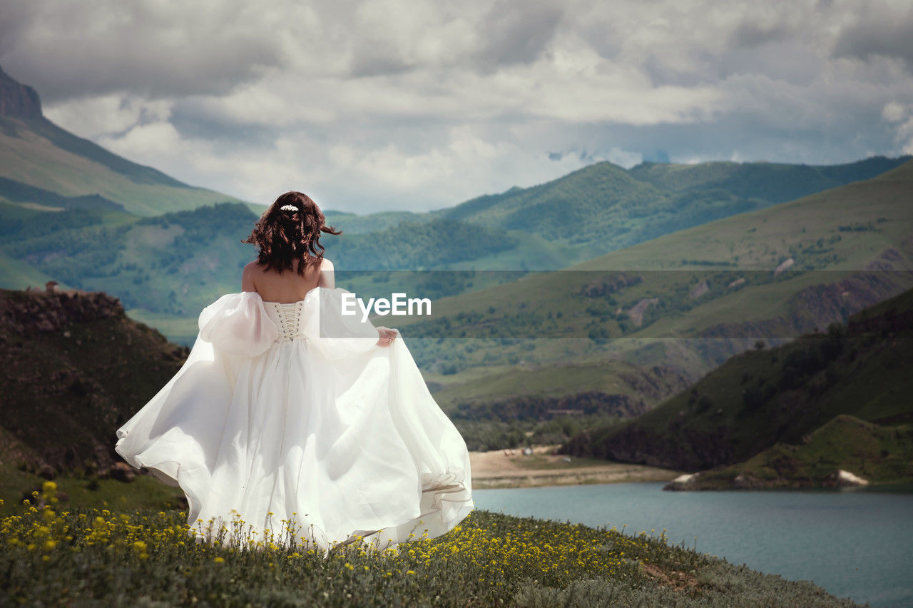 Bride in a white wedding dress walks in the green mountains on the grass, in the background there