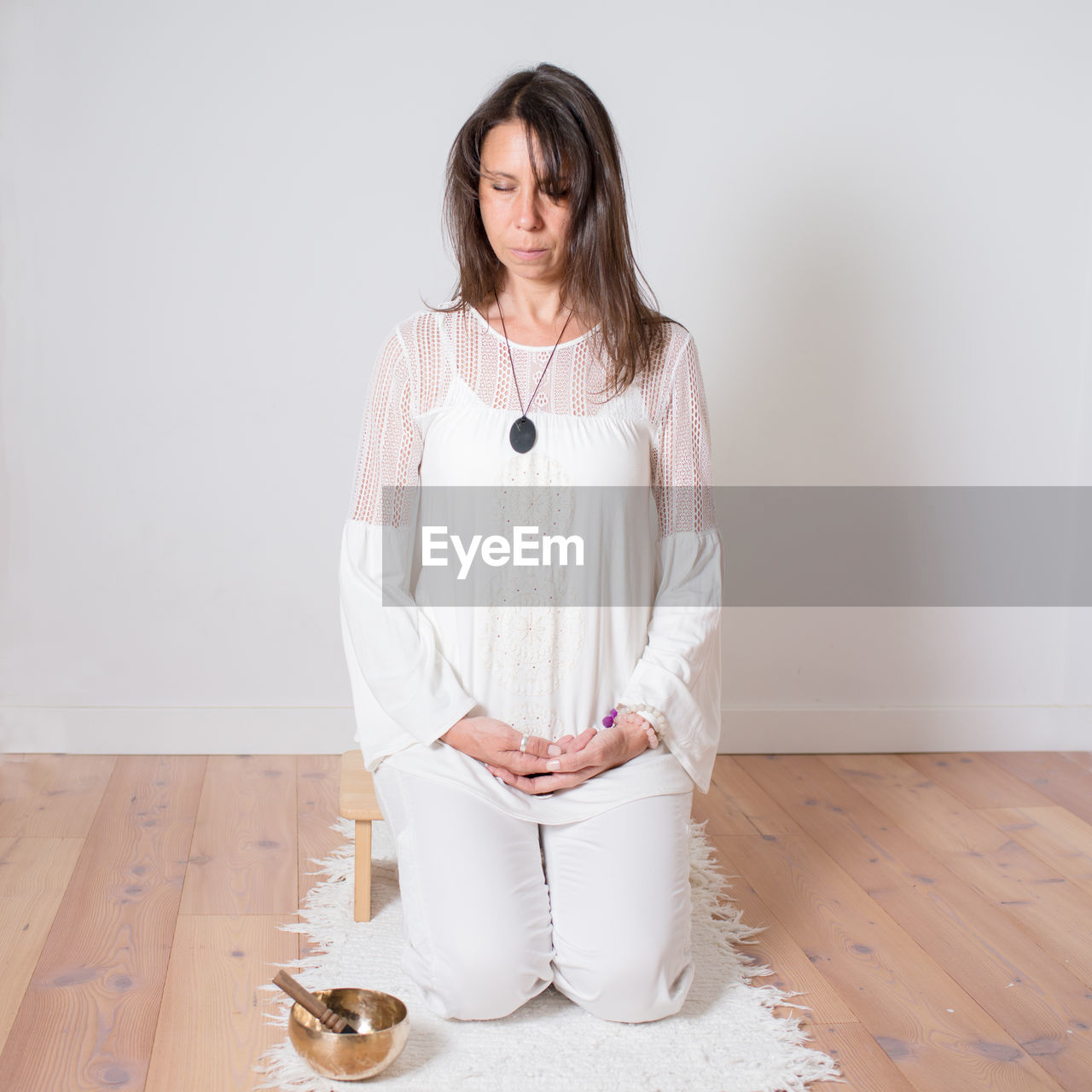 Adult caucasian woman dressed in white during a meditation sesion. metal singing bowl next to her.
