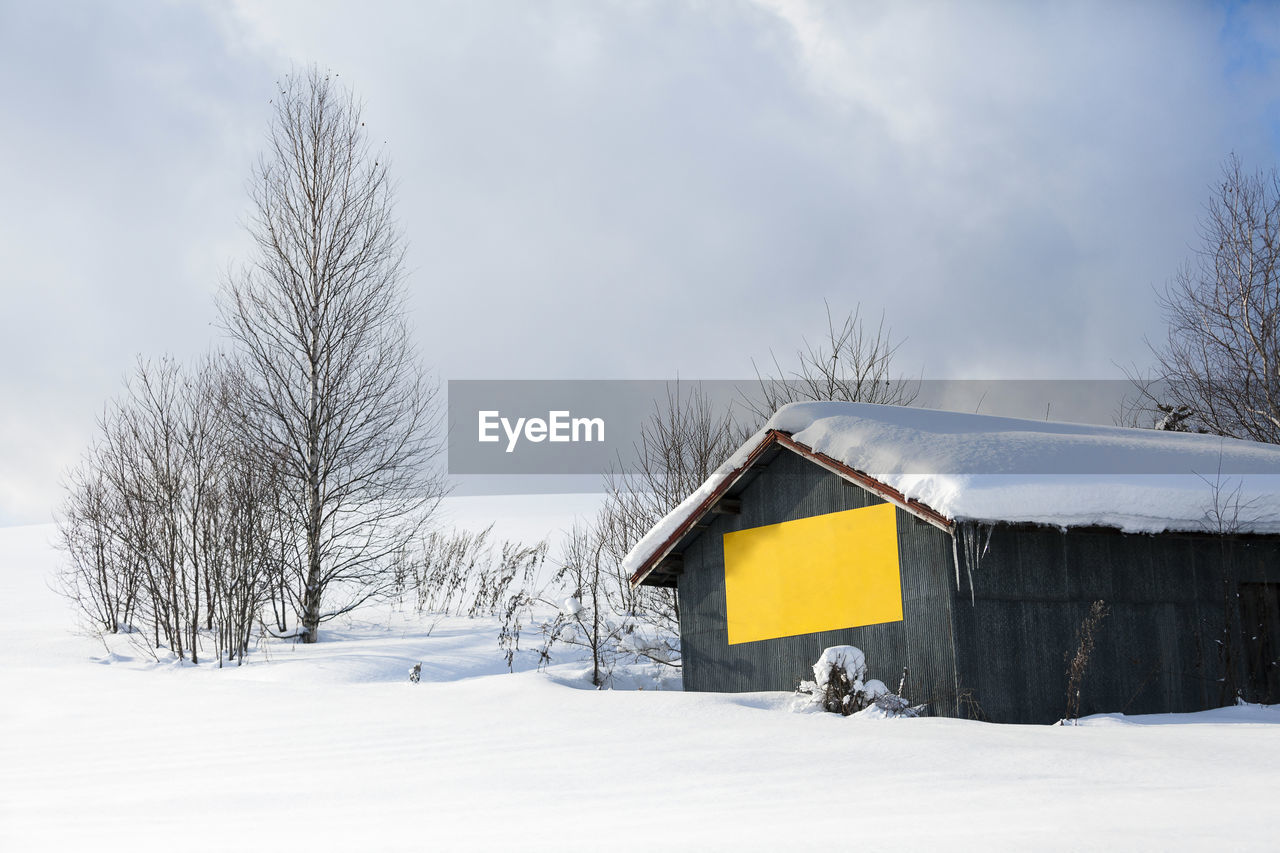 Snow covered house on field against sky during winter