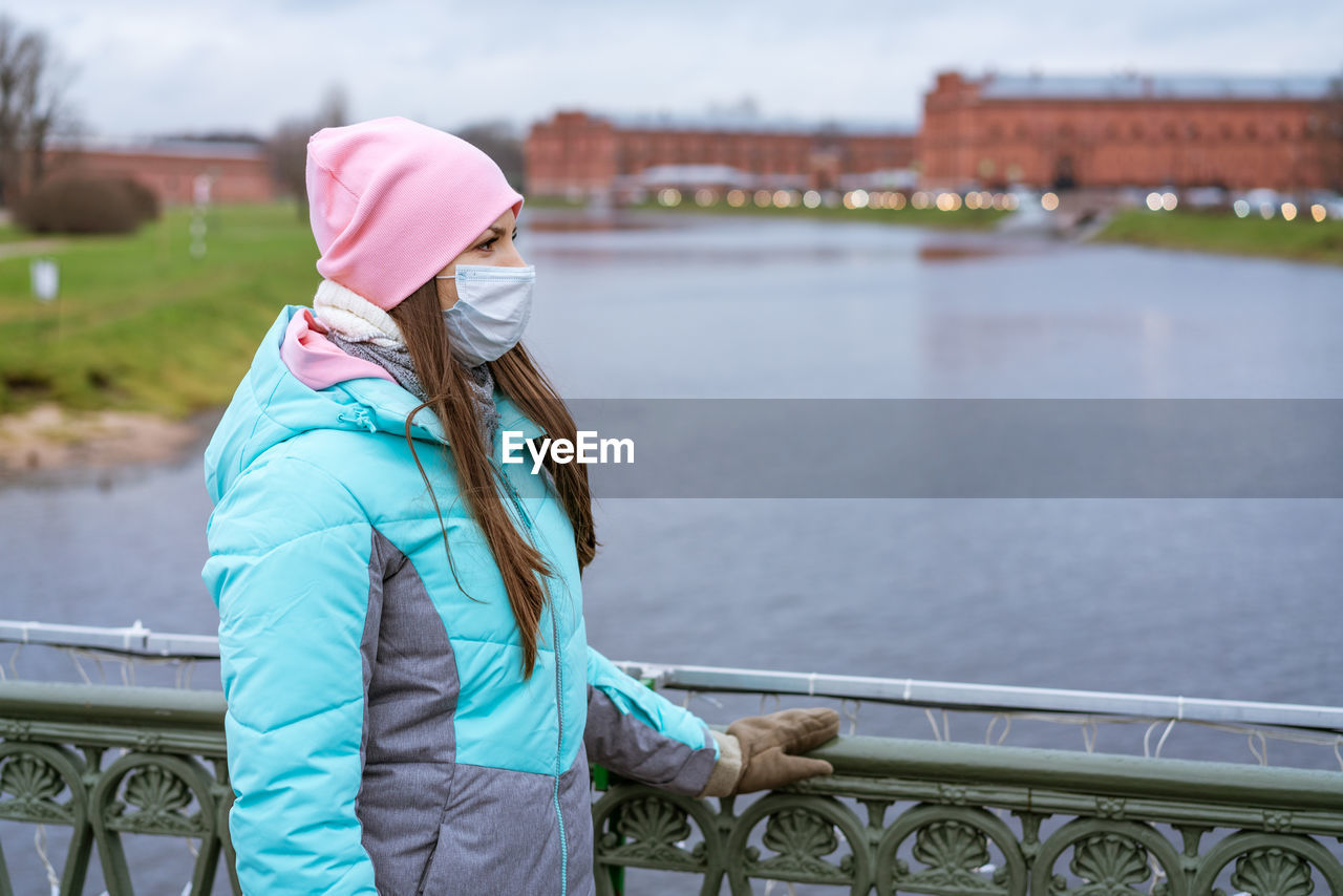 Young woman in a medical mask walks along the embankment in autumn