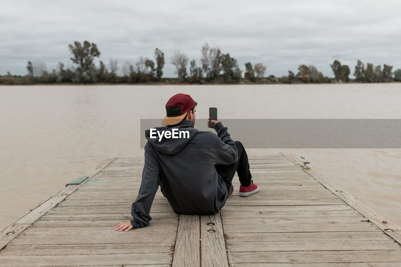 Rear view of woman sitting on pier against sky