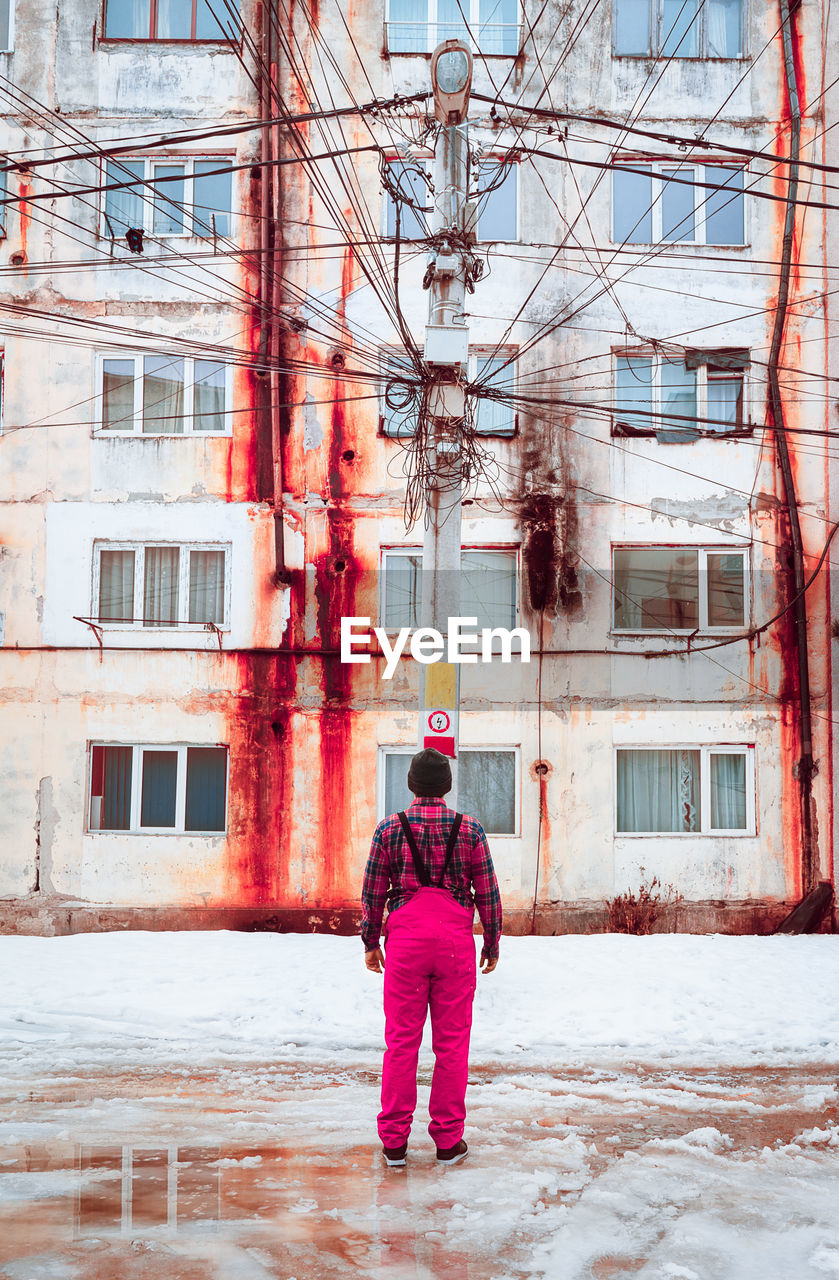 Rear view of man standing against abandoned building during winter