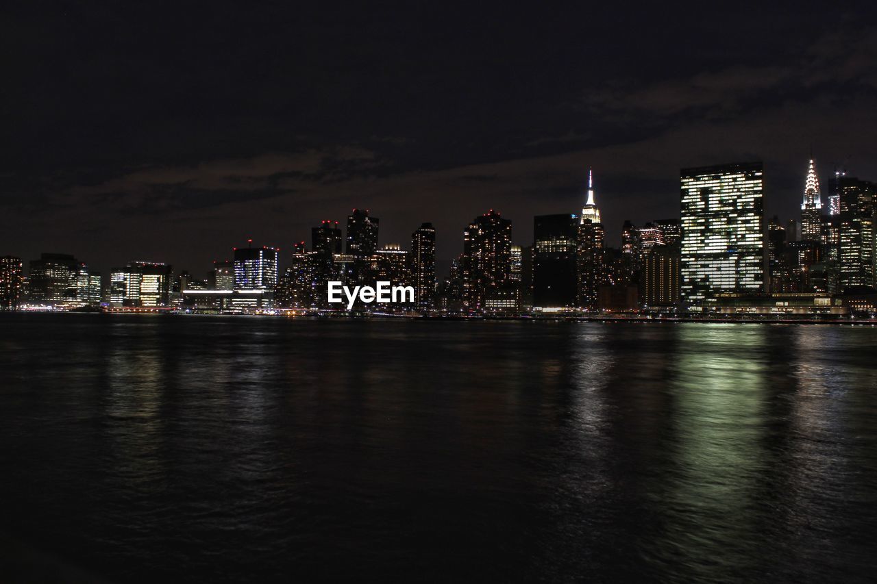 ILLUMINATED BUILDINGS BY RIVER AGAINST SKY