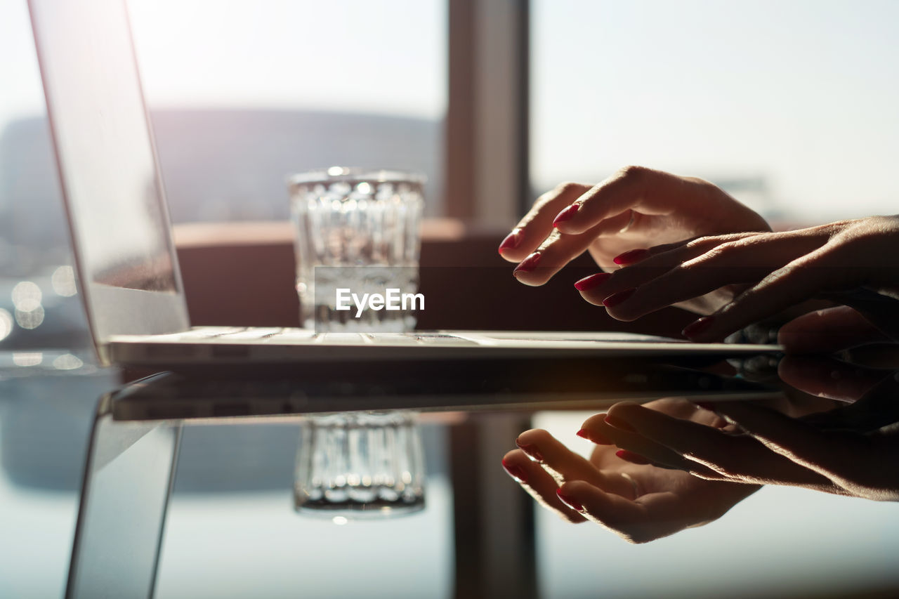 Close-up of woman using laptop at glass table