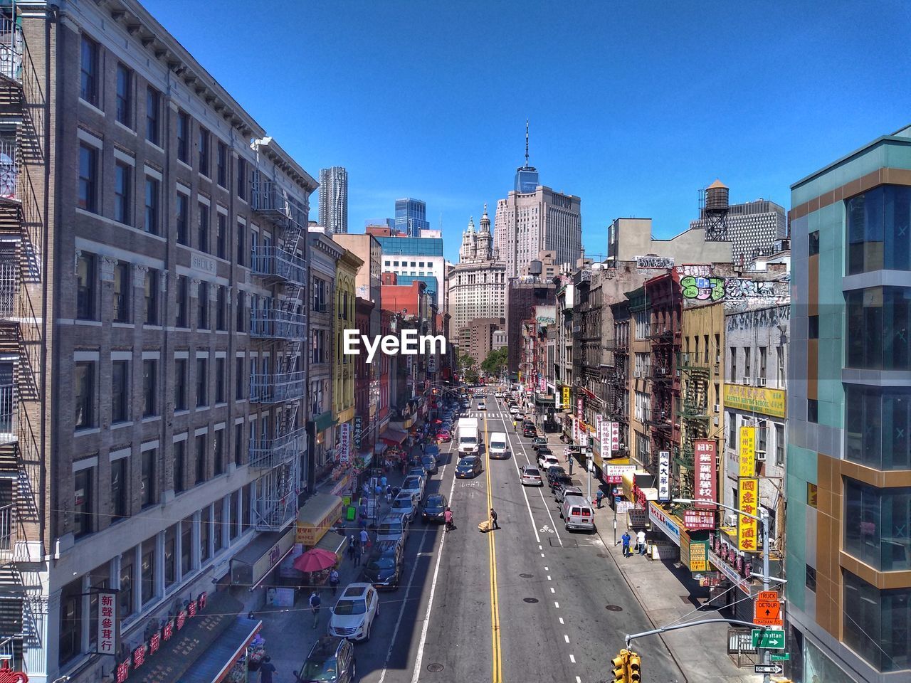 VEHICLES ON ROAD AMIDST BUILDINGS AGAINST SKY IN CITY