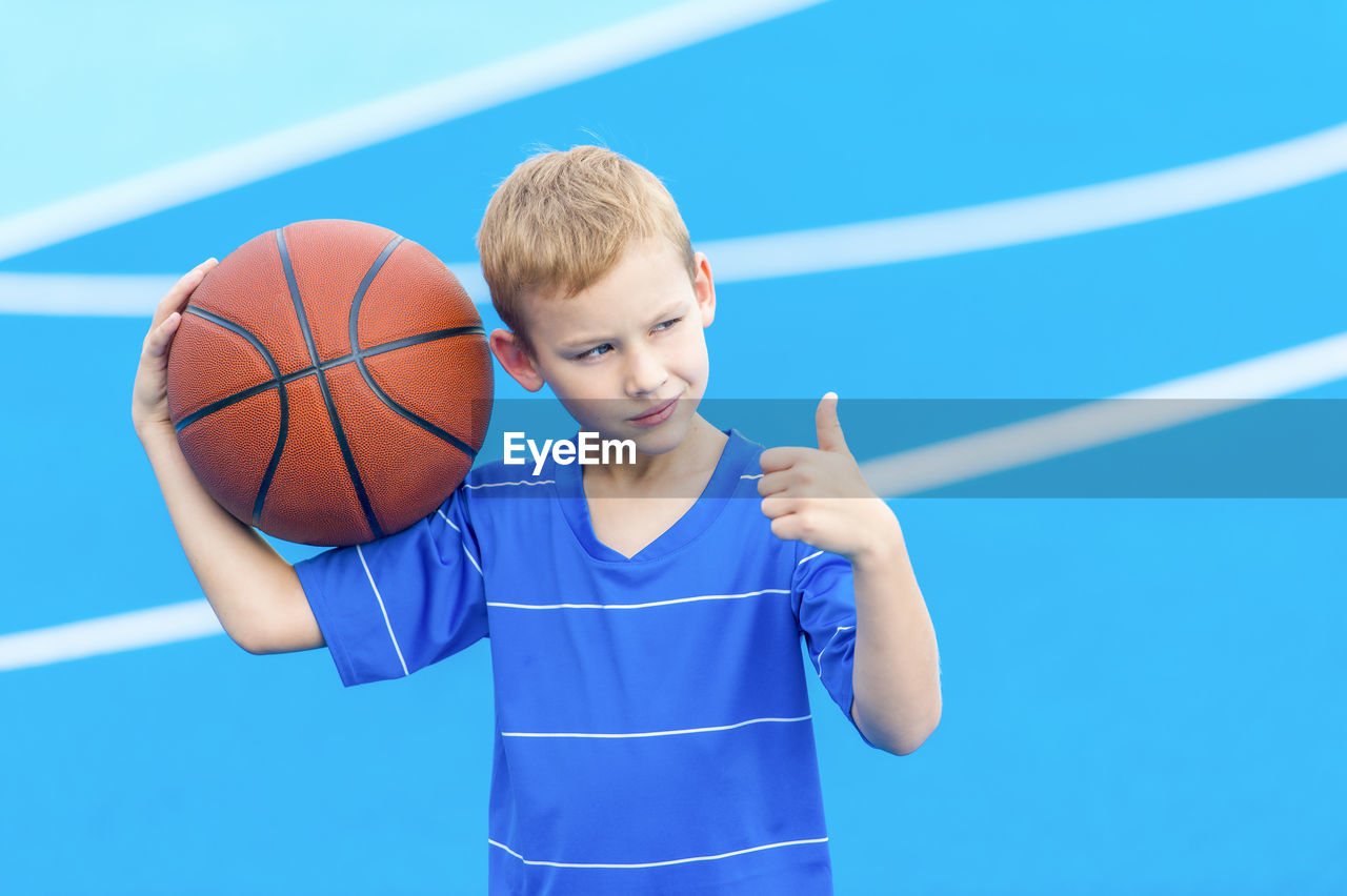 Boy gesturing and holding basketball while standing on sports court