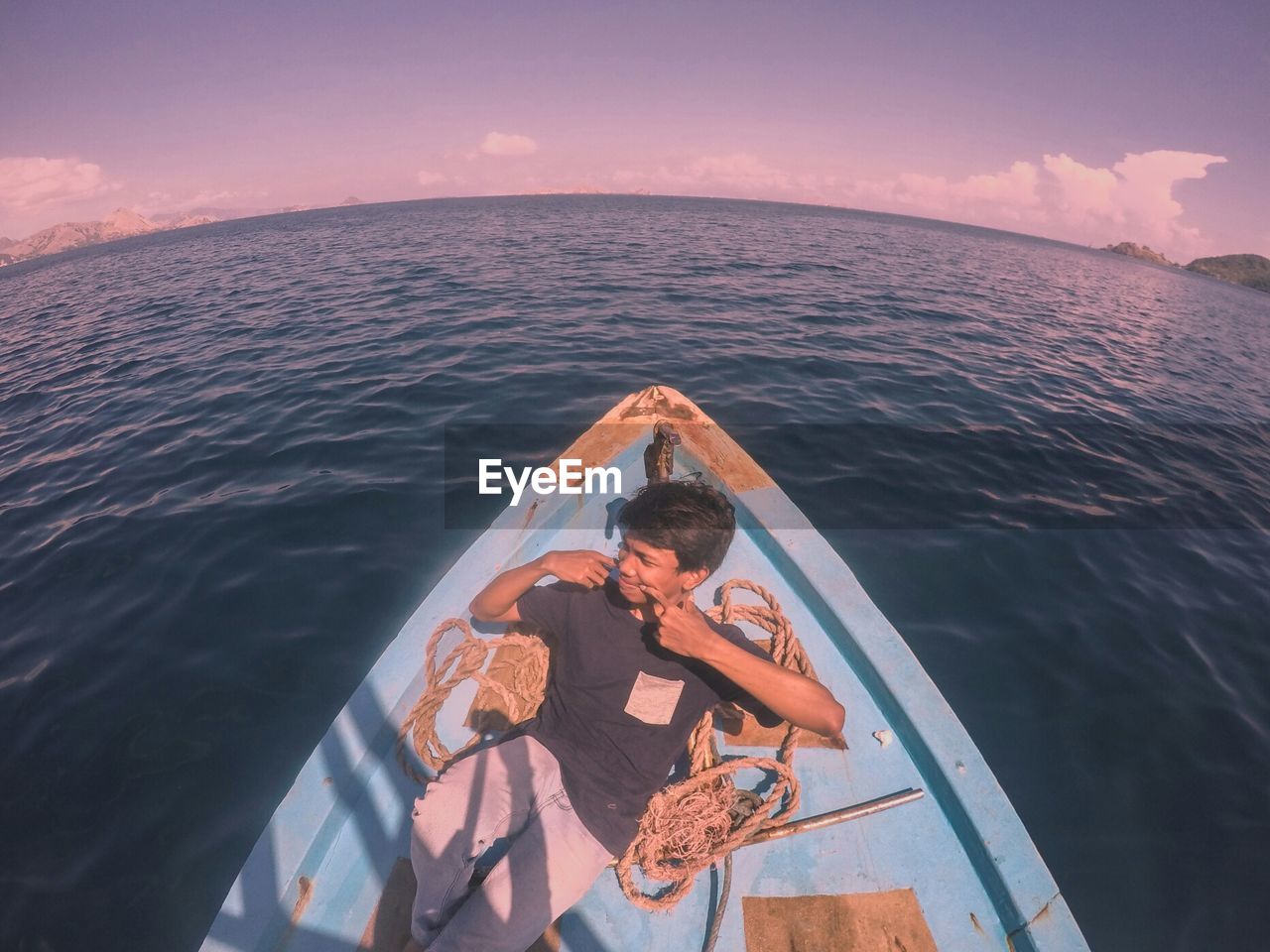 High angle view of young man looking away while sitting in boat on sea against sky during sunset