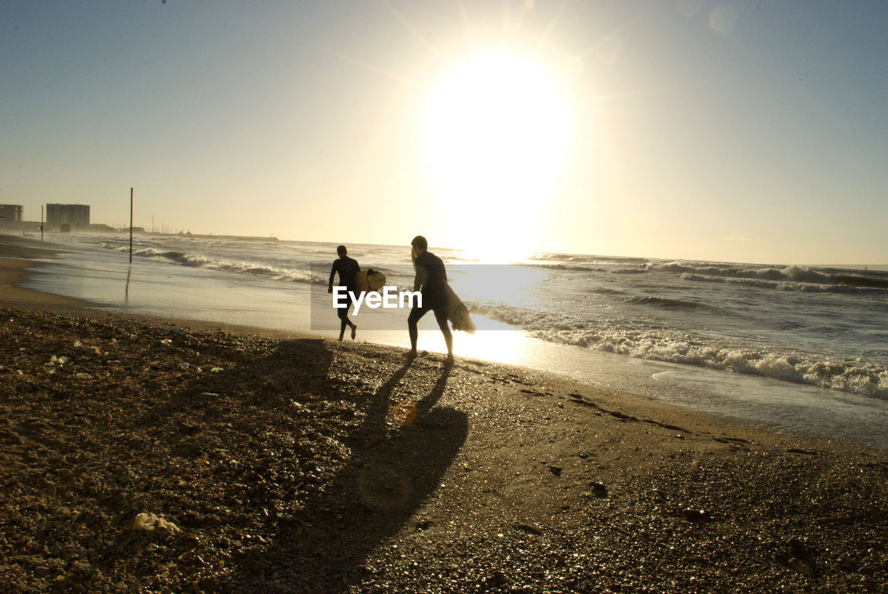 Silhouette people walking at beach against sky during sunset