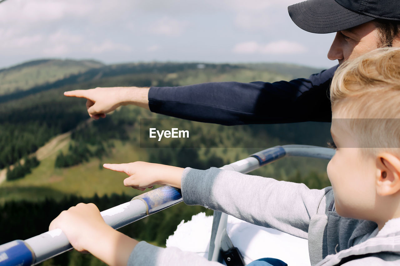 Close-up of father and son enjoying in ropeway ride in mountains and pointing in the distance.