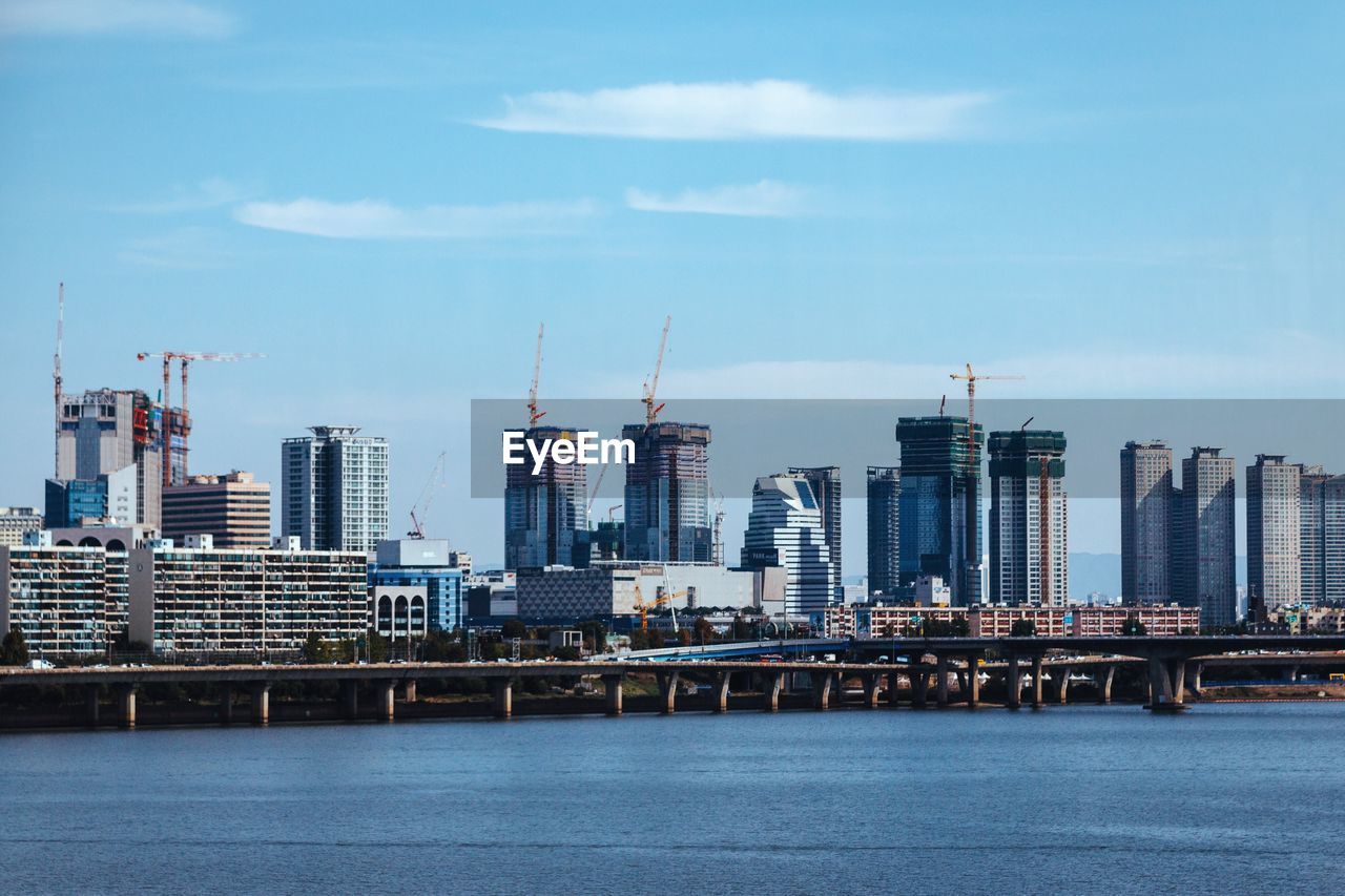 View of city at waterfront against cloudy sky