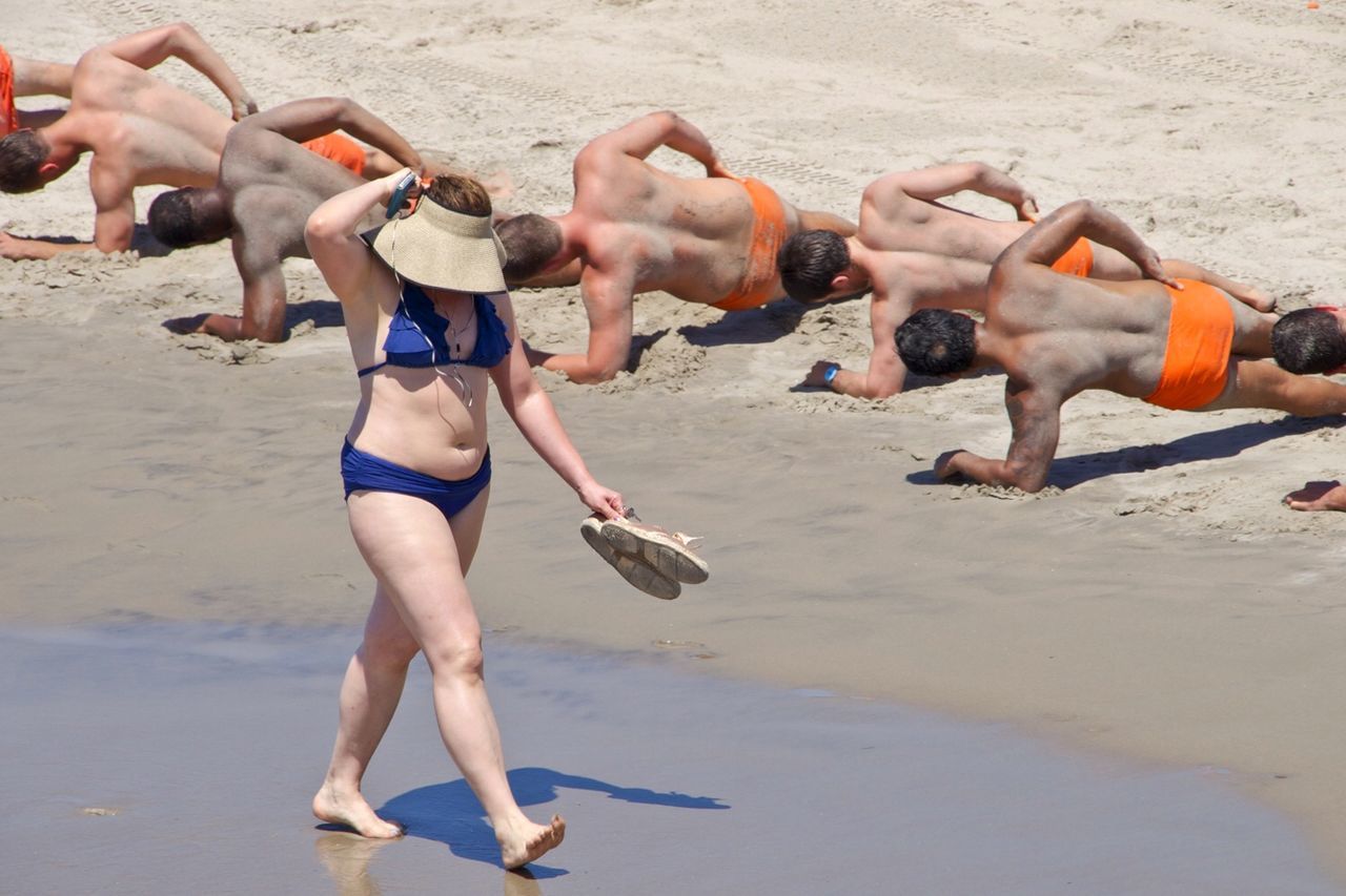 Woman walking along training men on beach