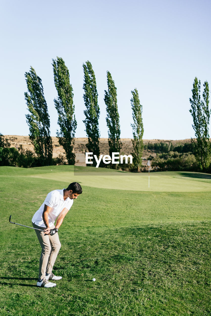 Professional male golf player preparing to hit ball with putter in green field while looking down on summer day