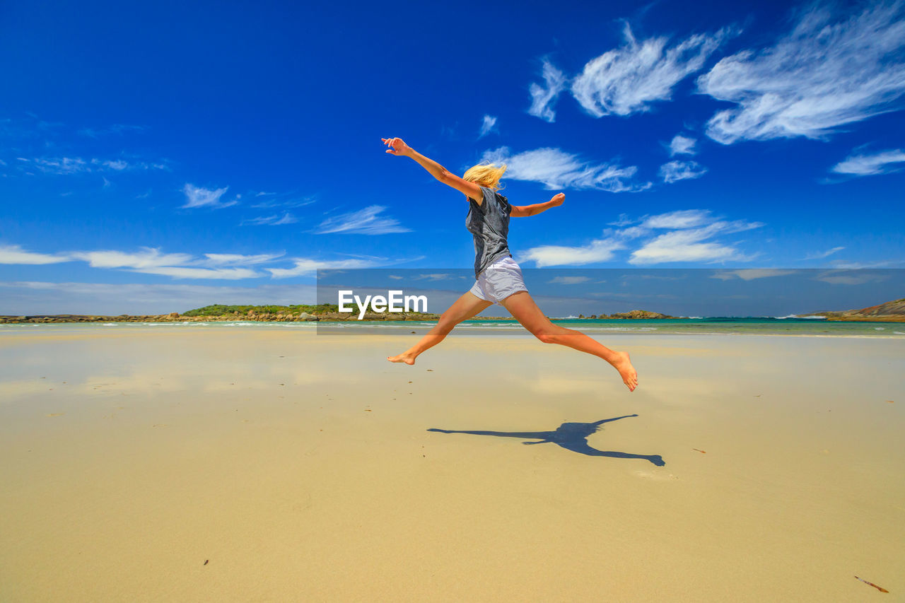 Low angle view of woman jumping at beach against blue sky