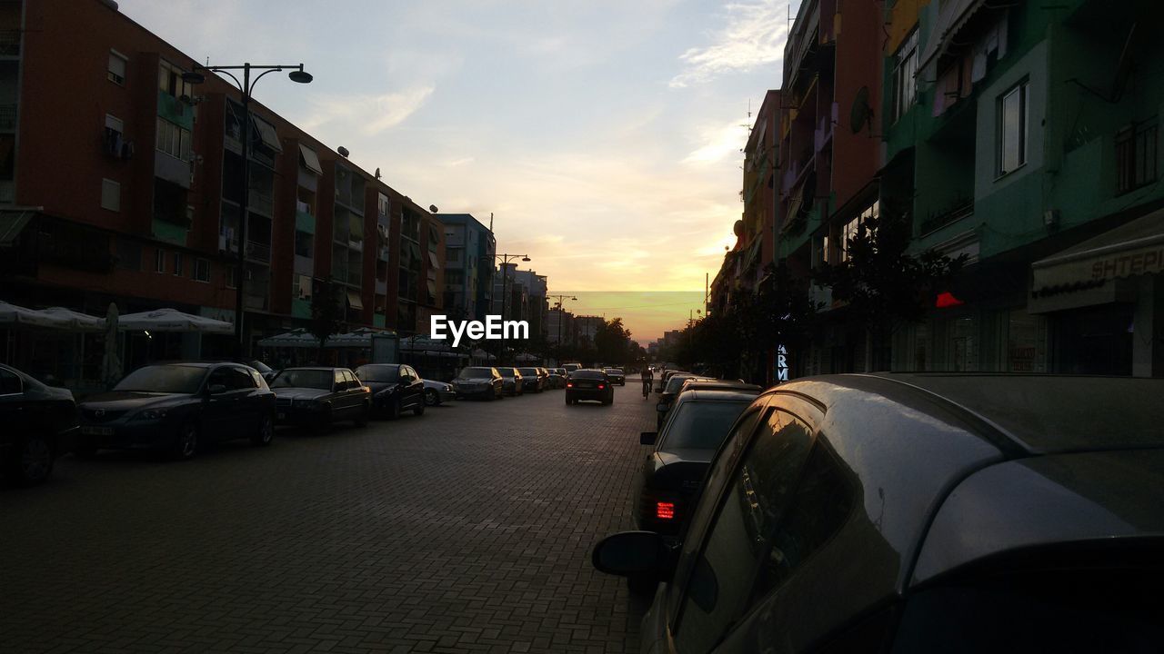 Cars parked on road by buildings against cloudy sky